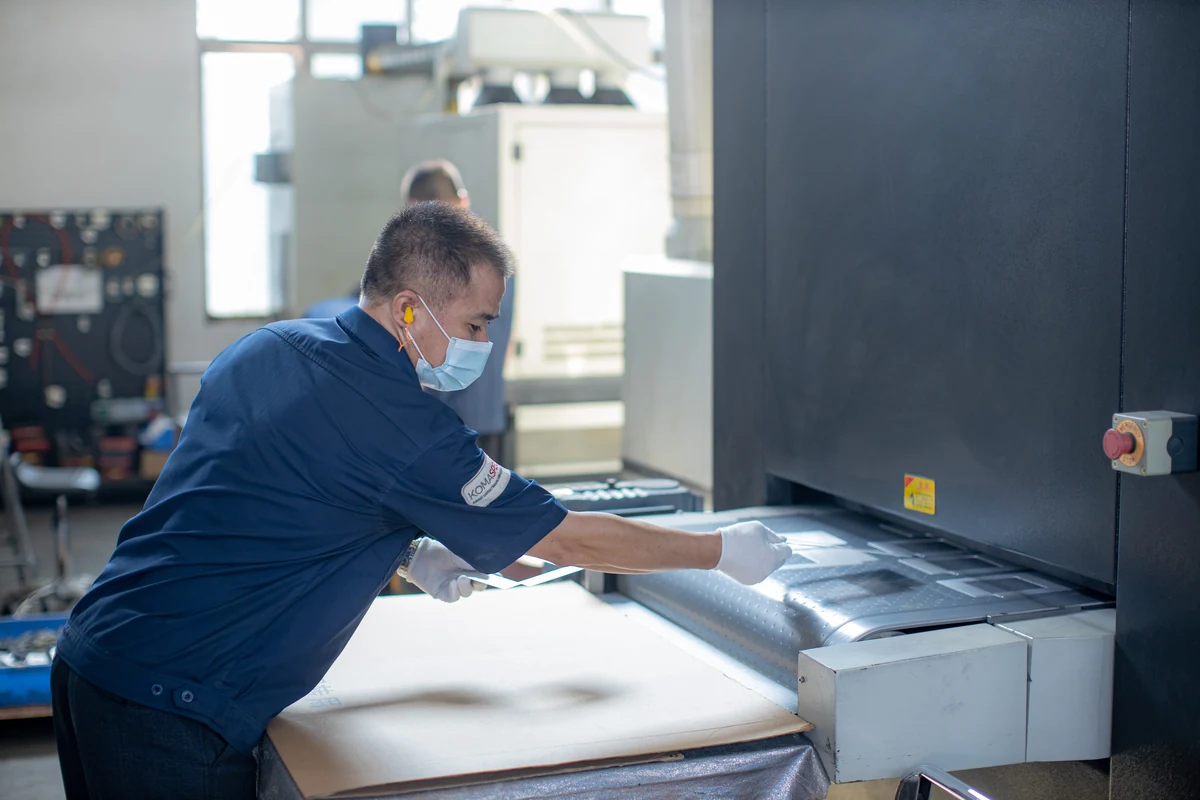 Komaspec technician wearing gloves and a mask deburring a stainless steel part on an in-line finishing machine