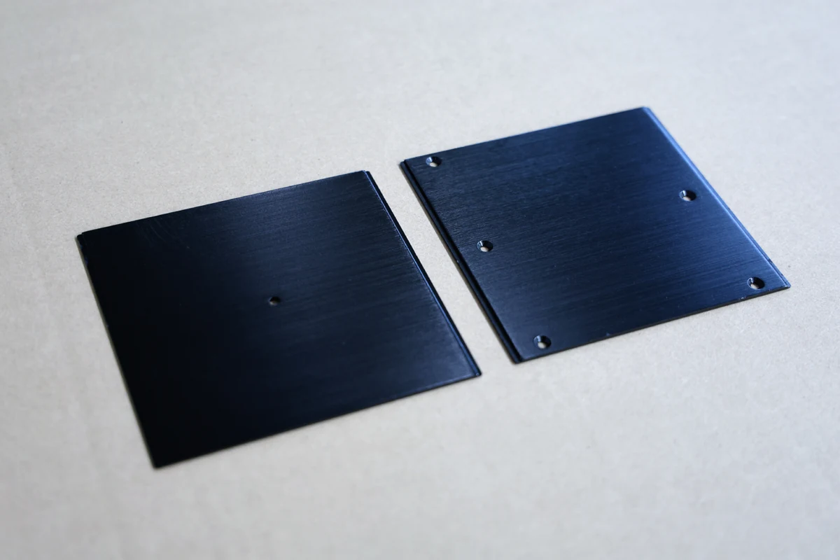 Two black anodized 5052 aluminum sheet metal panels with a brushed finish and laser-cut mounting holes