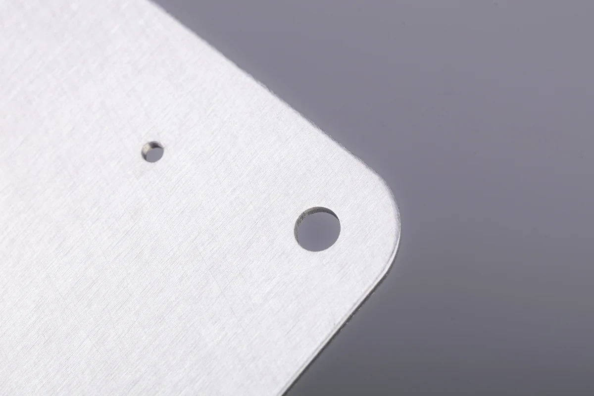 Close-up of a brushed stainless steel sheet metal corner with two punched mounting holes