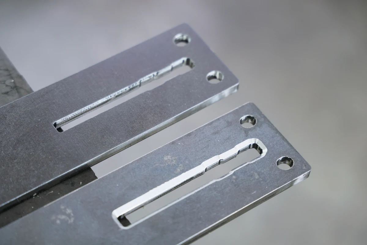 Two laser-cut steel plates with milled chamfers along the slot and at the hole edges