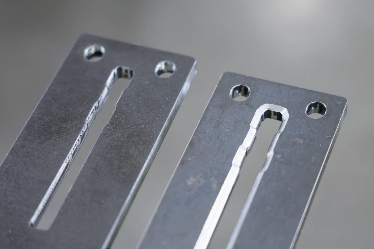 Close-up of a chamfered slot edge and chamfered hole rims on two laser-cut steel plates