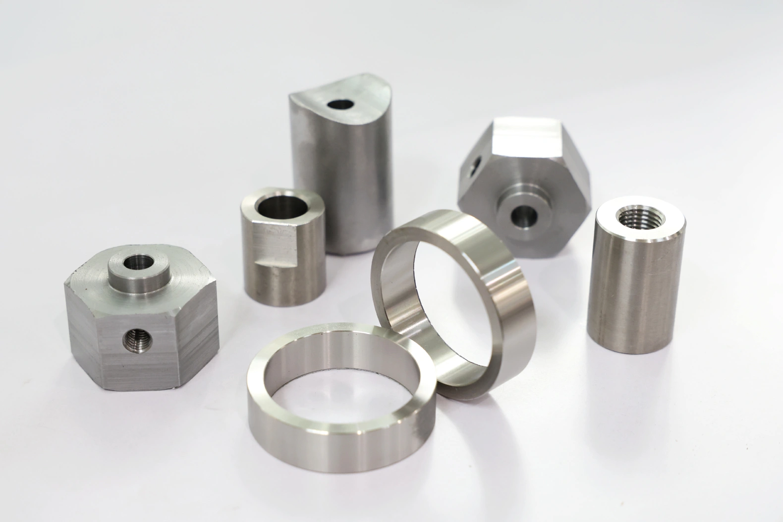 Assorted CNC turned metal parts including hex nuts, bushings, rings and a threaded standoff