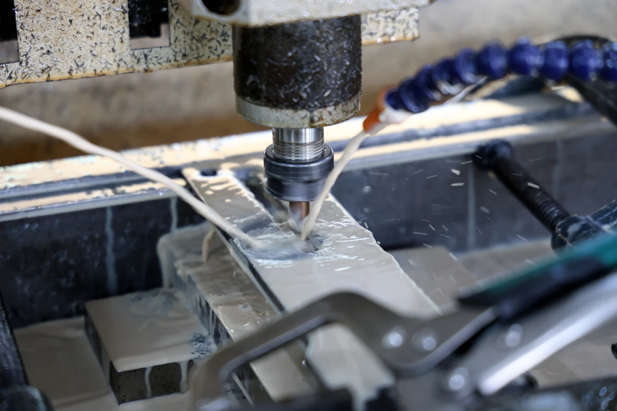 Milling machine cutting a chamfer along a slot in a clamped sheet metal part under flood coolant