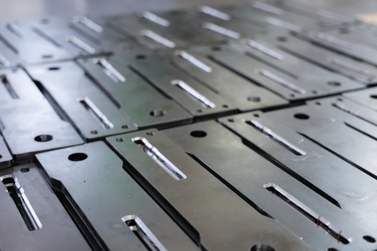 Laser-cut steel plates with 45-degree chamfered slot edges, stacked after chamfering