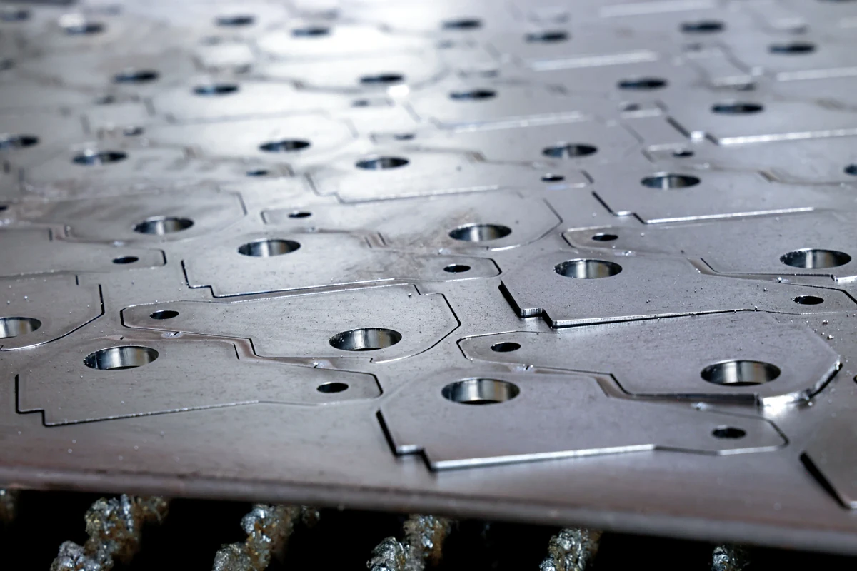 Macro view of a densely nested aluminum sheet metal pattern with laser-cut holes and slots close together