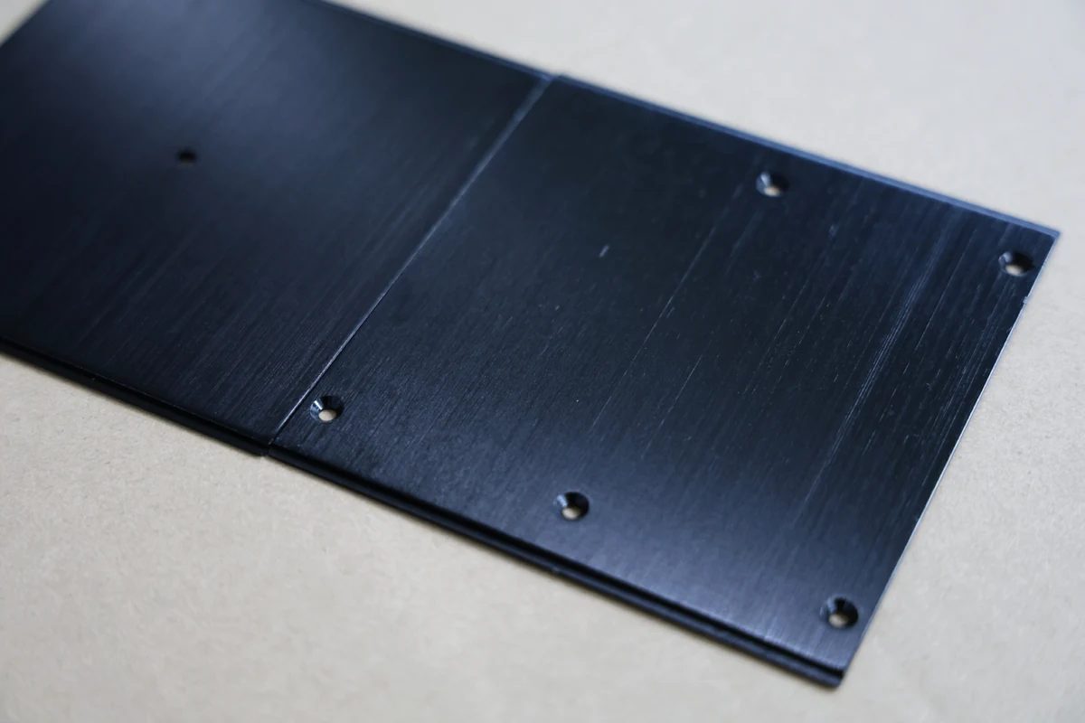 Close-up of black anodized aluminum panel edges showing brushed texture and precision-cut mounting holes
