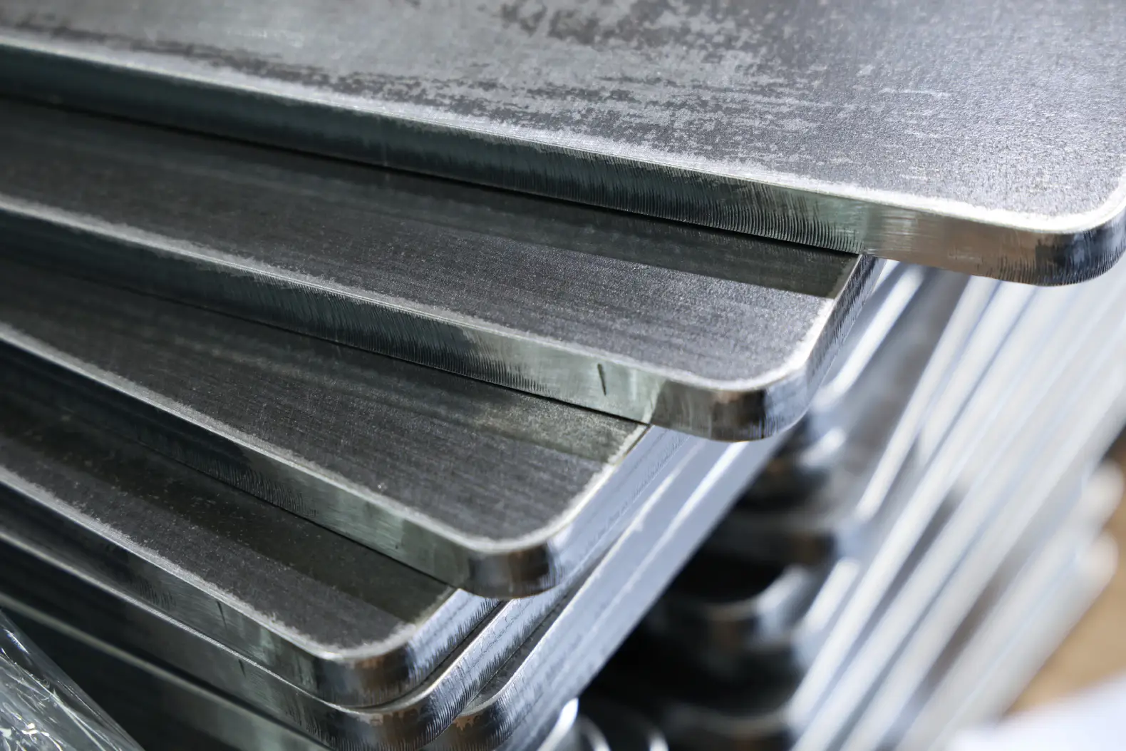 Stack of laser-cut hot rolled steel plate parts with bright cut edges, radiused corners and mill scale on the faces