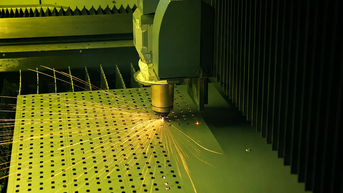 Fiber laser cutting a hole pattern into aluminum sheet, sparks flying from the kerf
