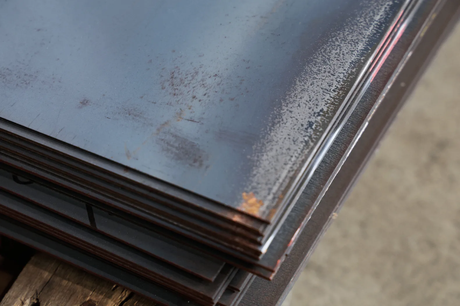 Close-up of hot rolled steel sheet showing blue-grey mill scale flaking from the surface with rust spots forming underneath