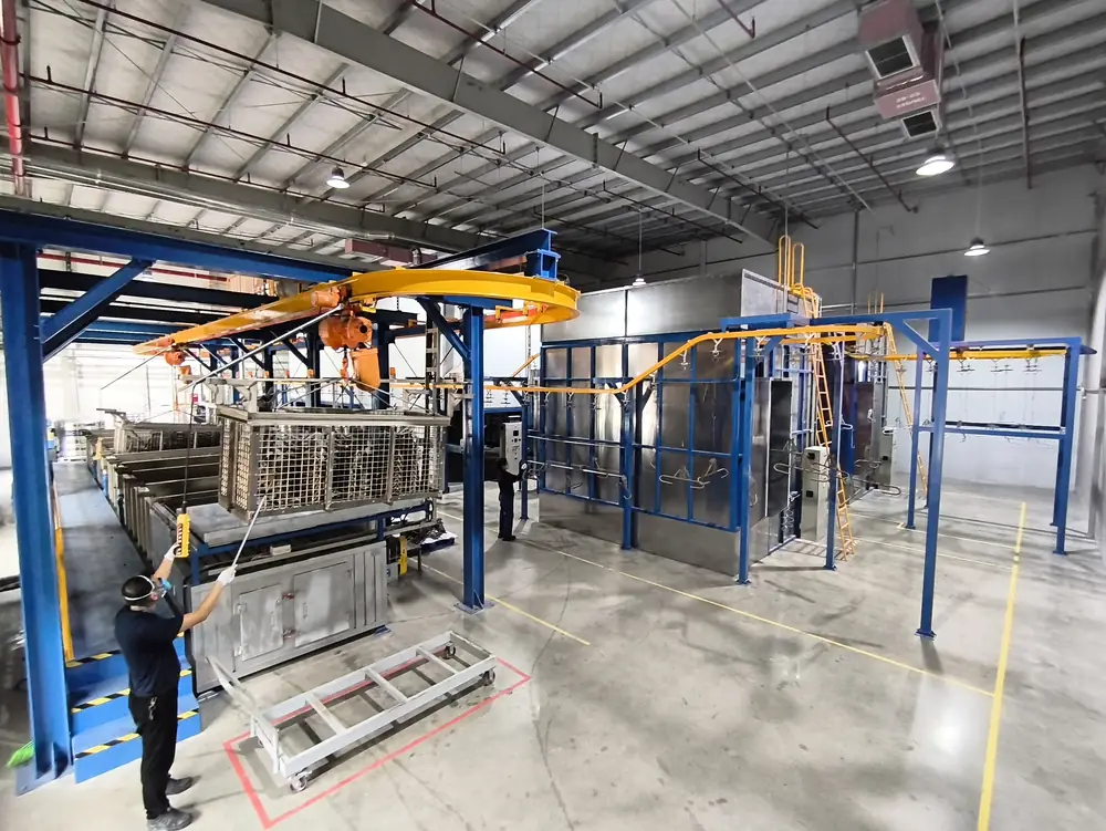 Wide view of a multi-stage industrial pretreatment line with an overhead conveyor and tank booths in a metal fabrication facility